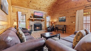 A wooden cabin interior with a fireplace, leather sofas, a television, and a table. - Serene Creek Cabin (Sevierville)