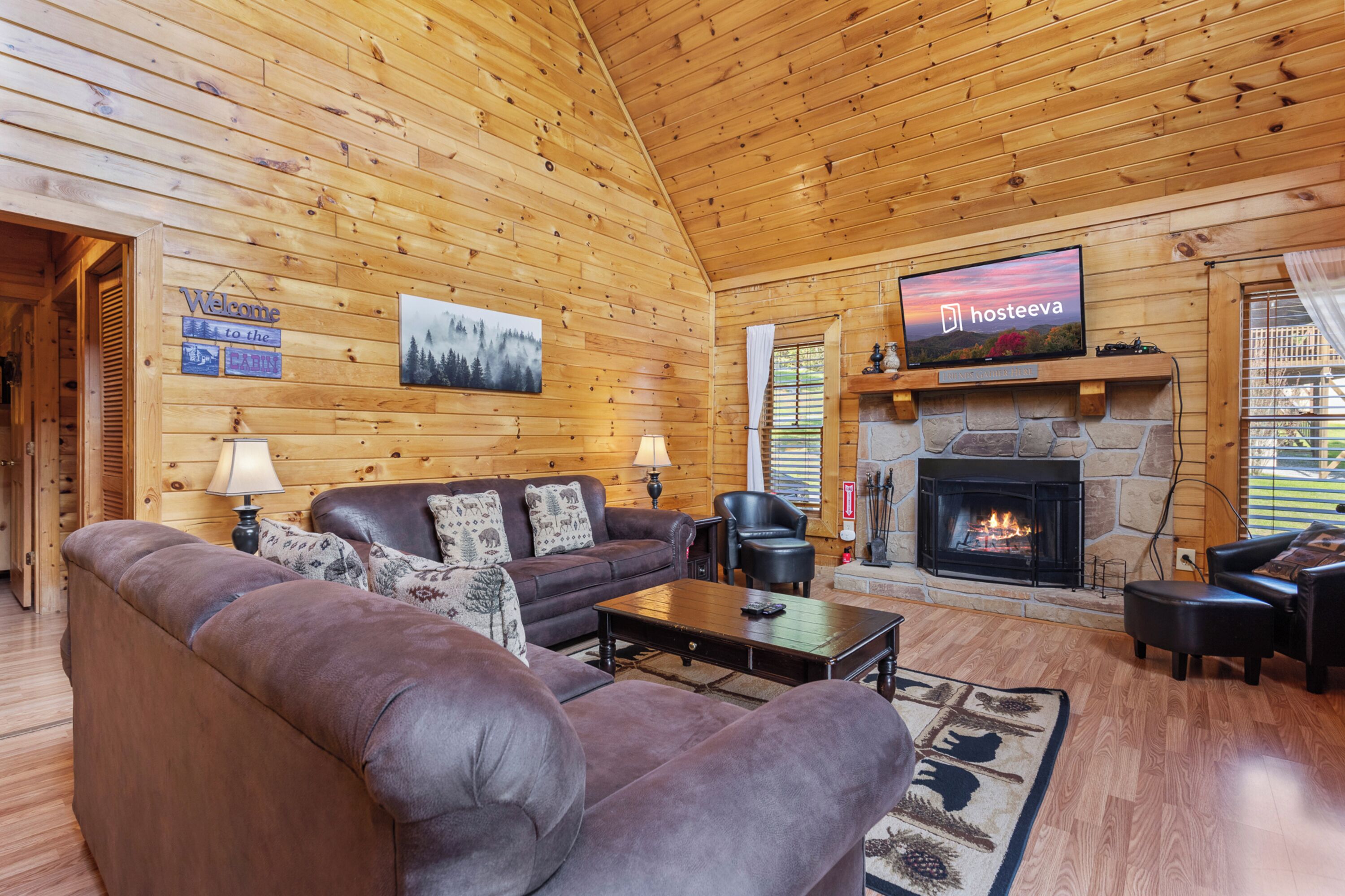 L’intérieur d’un chalet chaleureux, avec une cheminée, des murs en bois, un canapé et un téléviseur.