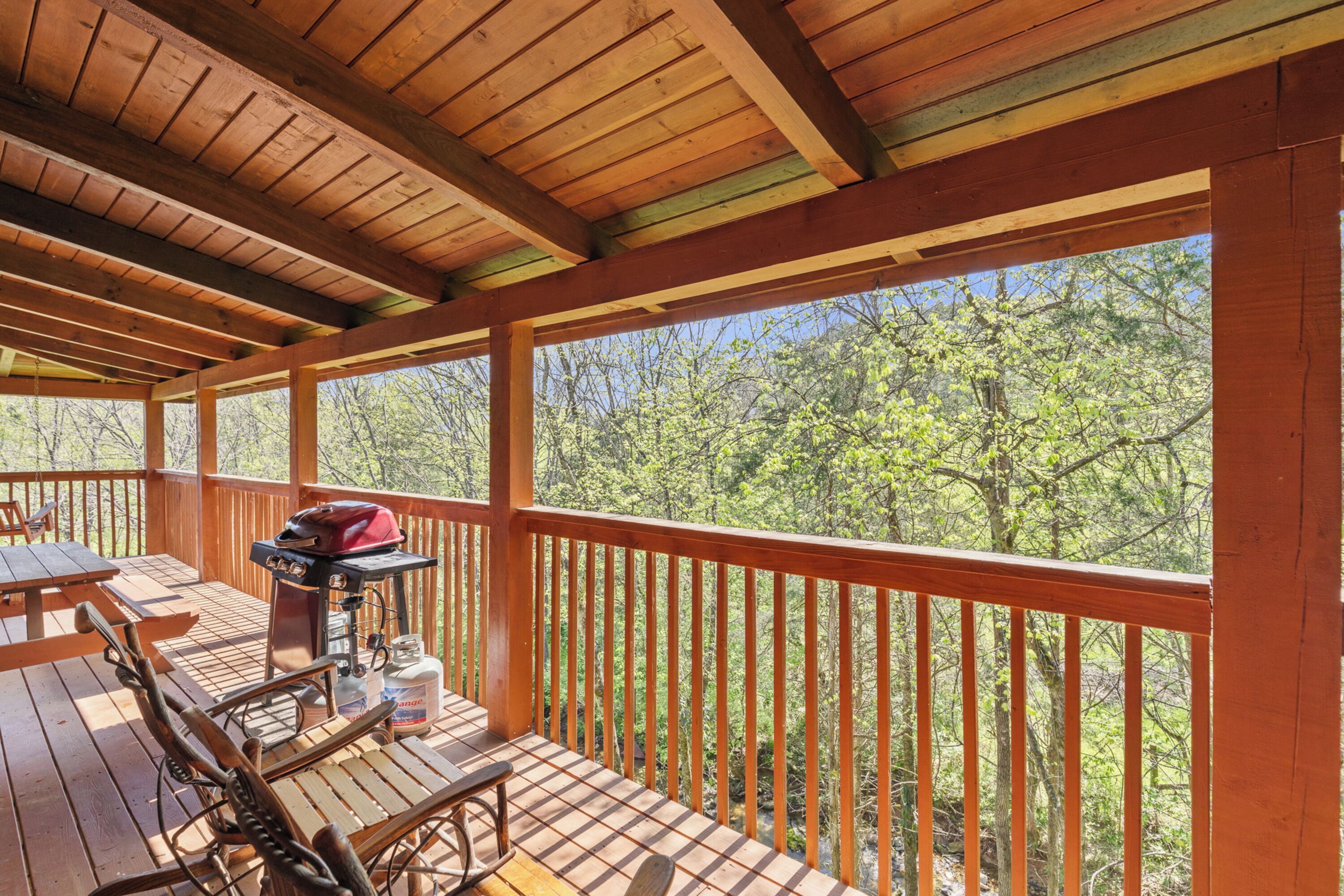 Eine Holzterrasse mit Picknicktischen und einem Grill, mit Blick auf ein bewaldetes Gebiet.
