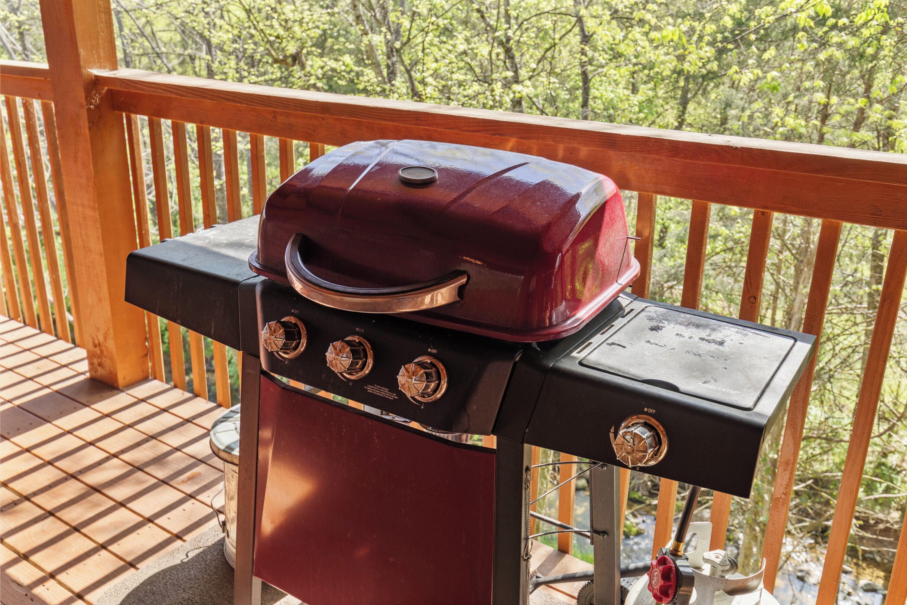 Un barbecue installé sur une terrasse en bois dotée d’une rambarde, le tout entouré d’arbres.