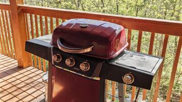 Una griglia barbecue su un pontile in legno con ringhiera, circondata da alberi.