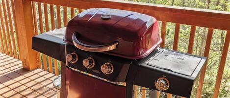 Un barbecue installé sur une terrasse en bois dotée d’une rambarde, le tout entouré d’arbres.