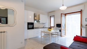 A modern kitchen with white cabinets, a dining area with a table and chairs, a sofa with red cushions, and a television. - Nice apartment for 5 guests with WIFI, A/C, TV, terrace and pets allowed (San Bartolomeo Al Mare)