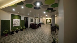 A hotel lobby with a green wall, a reception desk, seating area, and a patterned floor. - MURALI KRISHNA APART HOTEL (Kakinada)