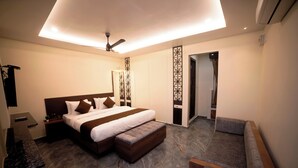 A modern bedroom with a large bed, bedside tables, a bench, a ceiling fan, and a door leading to a bathroom. - MURALI KRISHNA APART HOTEL (Kakinada)