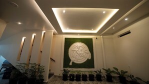 A modern interior with a recessed ceiling, a green wall with a circular relief, and potted plants along the wall. - MURALI KRISHNA APART HOTEL (Kakinada)