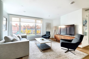 A modern living room with a sofa, armchair, coffee table, and TV. - Modern 2br-newly Built-near NYC (Hoboken)