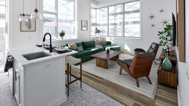 Un soggiorno moderno con un divano verde, un tavolino in legno e un angolo cottura con lavello e piano di lavoro.