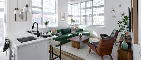 Una sala de estar moderna con un sofá verde, una mesa de centro de madera y una cocina con un lavamanos y encimera.