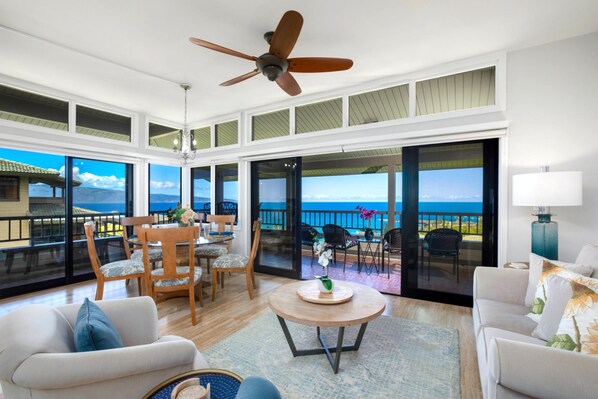 A spacious living room with a large balcony, wooden furniture, and a view of the ocean.