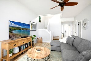 En moderne stue med et fladskærms-TV, en grå sofa, et træbord og en loftventilator.