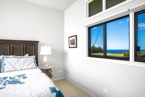 Et soveværelse med en seng, et natbord, en lampe, et billede i ramme og et vindue med havudsigt.