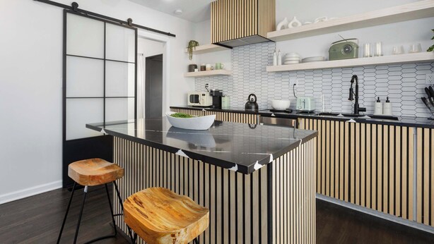 Une cuisine moderne avec un îlot central, des tabourets en bois et un plan de travail noir.