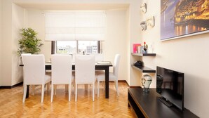 Un comedor con una mesa y sillas, una planta en maceta, una ventana con persianas, un televisor y un cuadro en la pared.