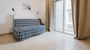 A modern living room with a patterned sofa, a small table, and a sliding glass door leading to a balcony.