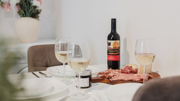 A dining table with white plates, two wine glasses, a bottle of wine, and a wooden board with sliced meats.