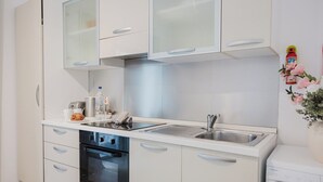 A compact kitchen with white cabinets, a stainless steel sink, a built-in oven, and a coffee maker.