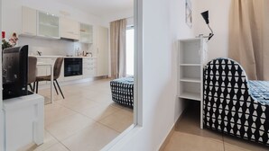 A modern kitchen with white cabinets, a dining area with a patterned table, and a TV on a stand.