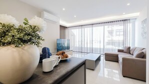 Una sala de estar moderna con un sofá, una mesa de centro y un televisor. Hay un jarrón grande con flores en la encimera.