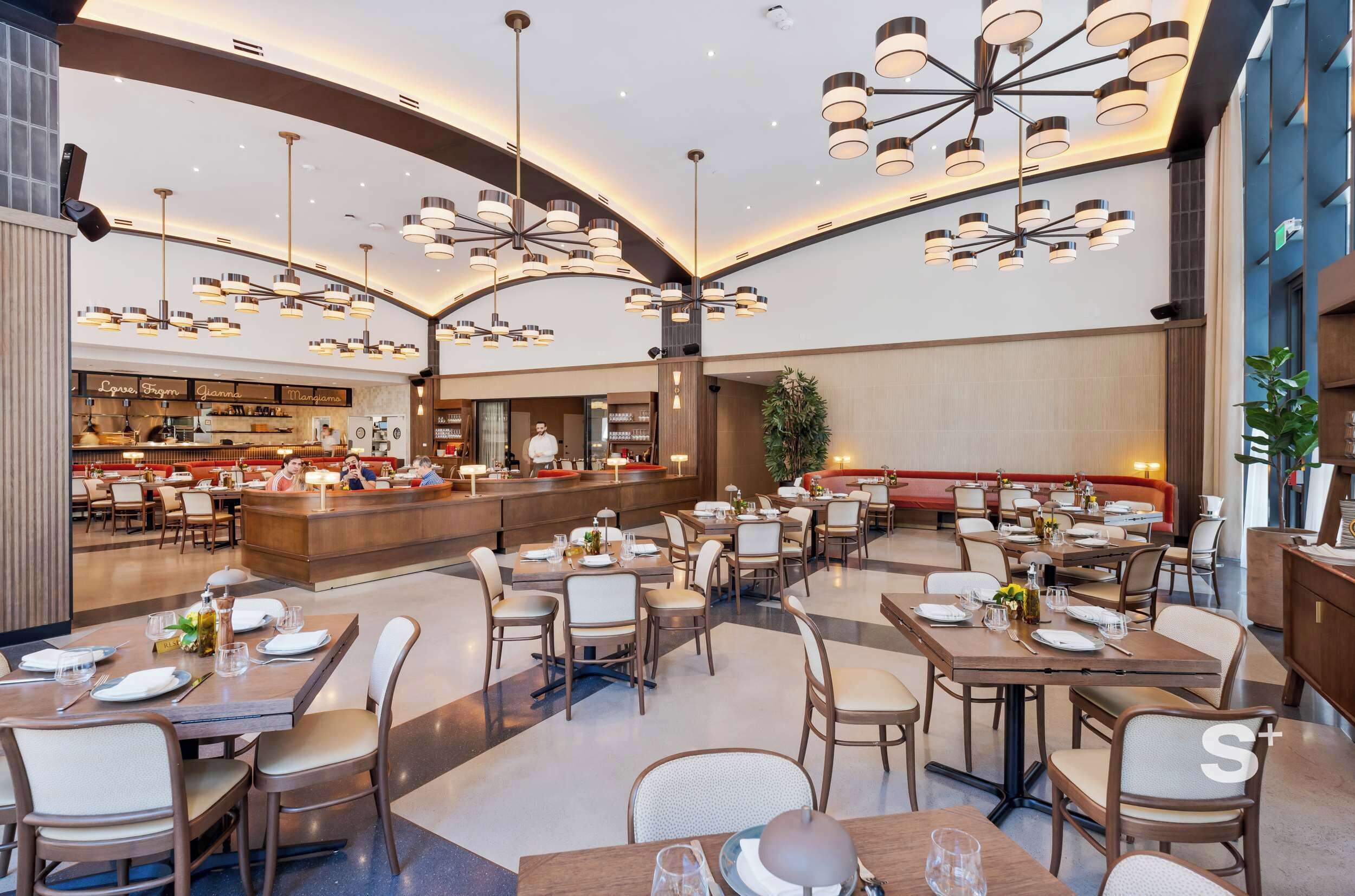 A spacious restaurant with multiple dining areas, a central bar, and modern lighting fixtures.