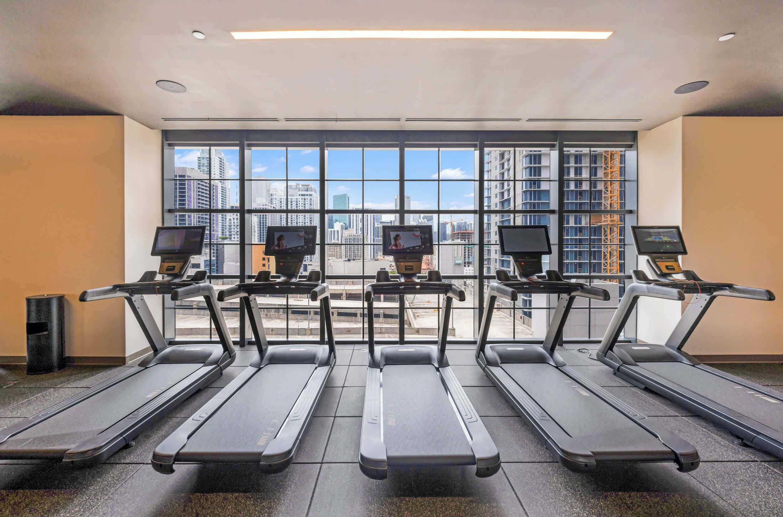 A gym with treadmills, large windows, and a view of the cityscape.
