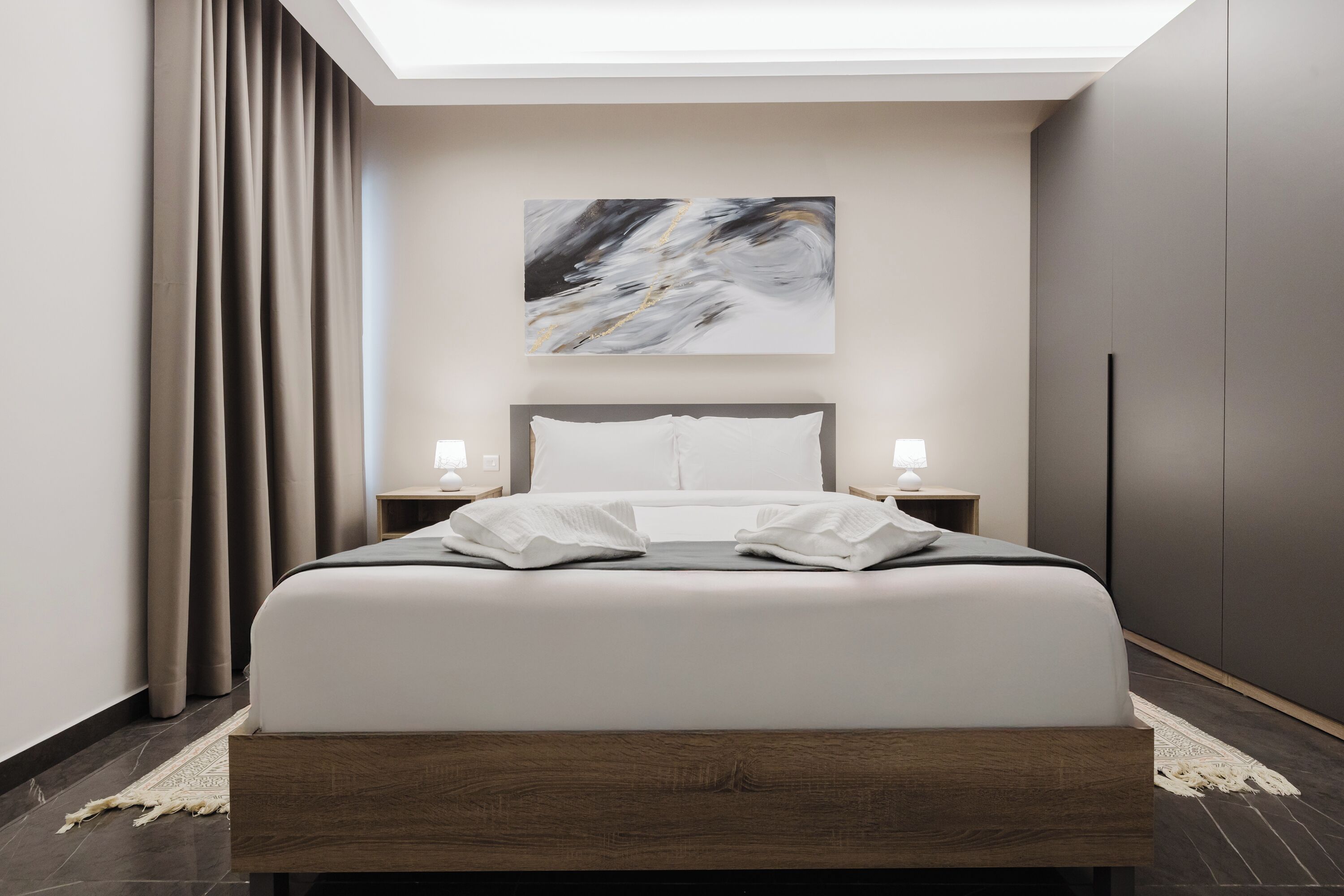 A modern hotel room with a large bed, a skylight, a painting on the wall, and a nightstand with a lamp.