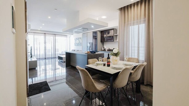 A modern dining area with a large table, chairs, and a kitchen in the background. - Enjoy a stylish experience at this centrally-located place. Enjoy easy access to Qawra promenade only seconds away from parks and the aquarium.  Modern and stylish, this apartment in Qawra is the ideal place to spend a holiday. (San Pawl il-Baħar)
