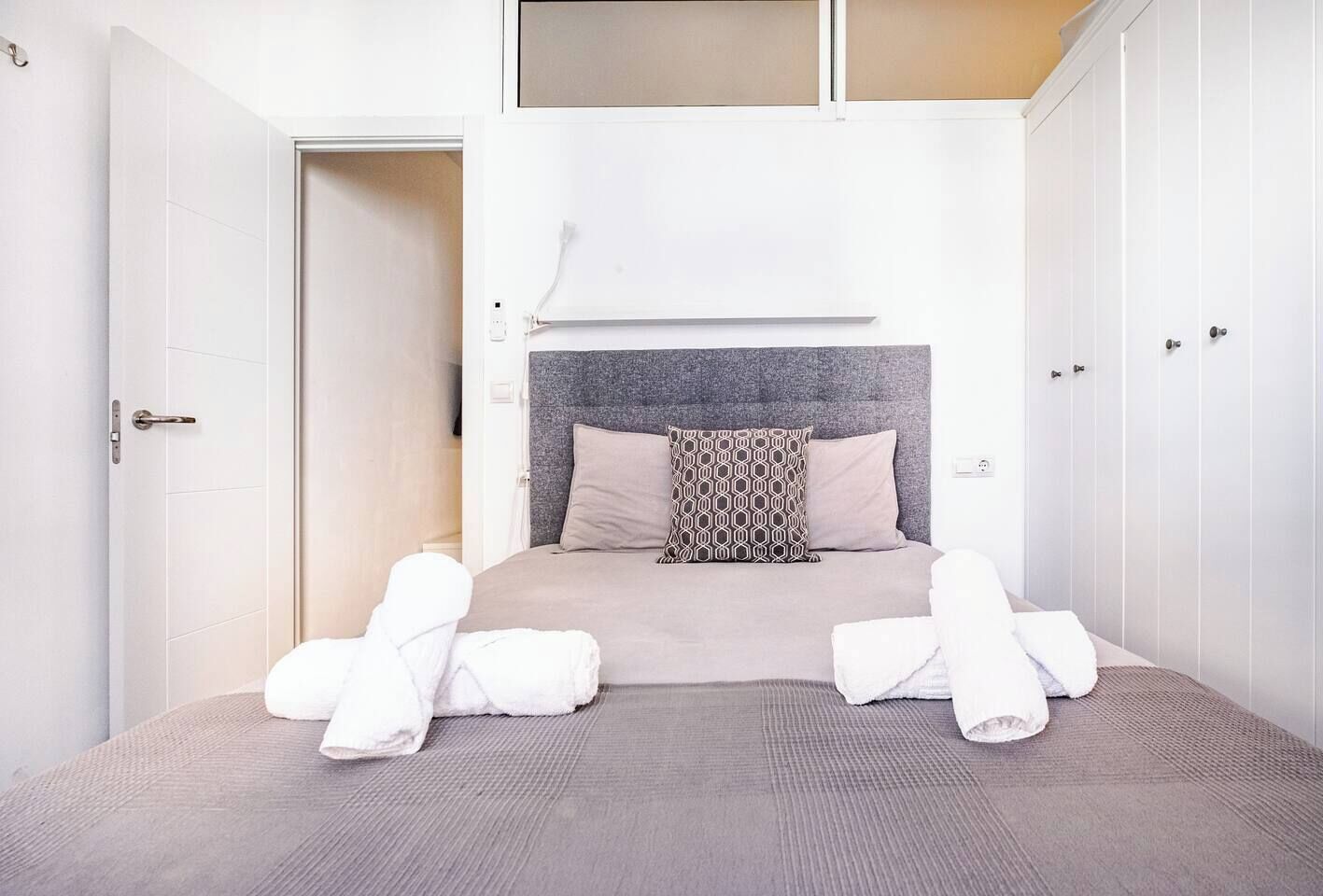 A hotel room with a bed, two white doors, and a window.