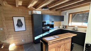 A modern kitchen with wooden beams, a large refrigerator, and a dining area with a wooden table.