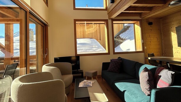 A high-ceilinged wooden interior with large windows, a sofa, a table, and a television.