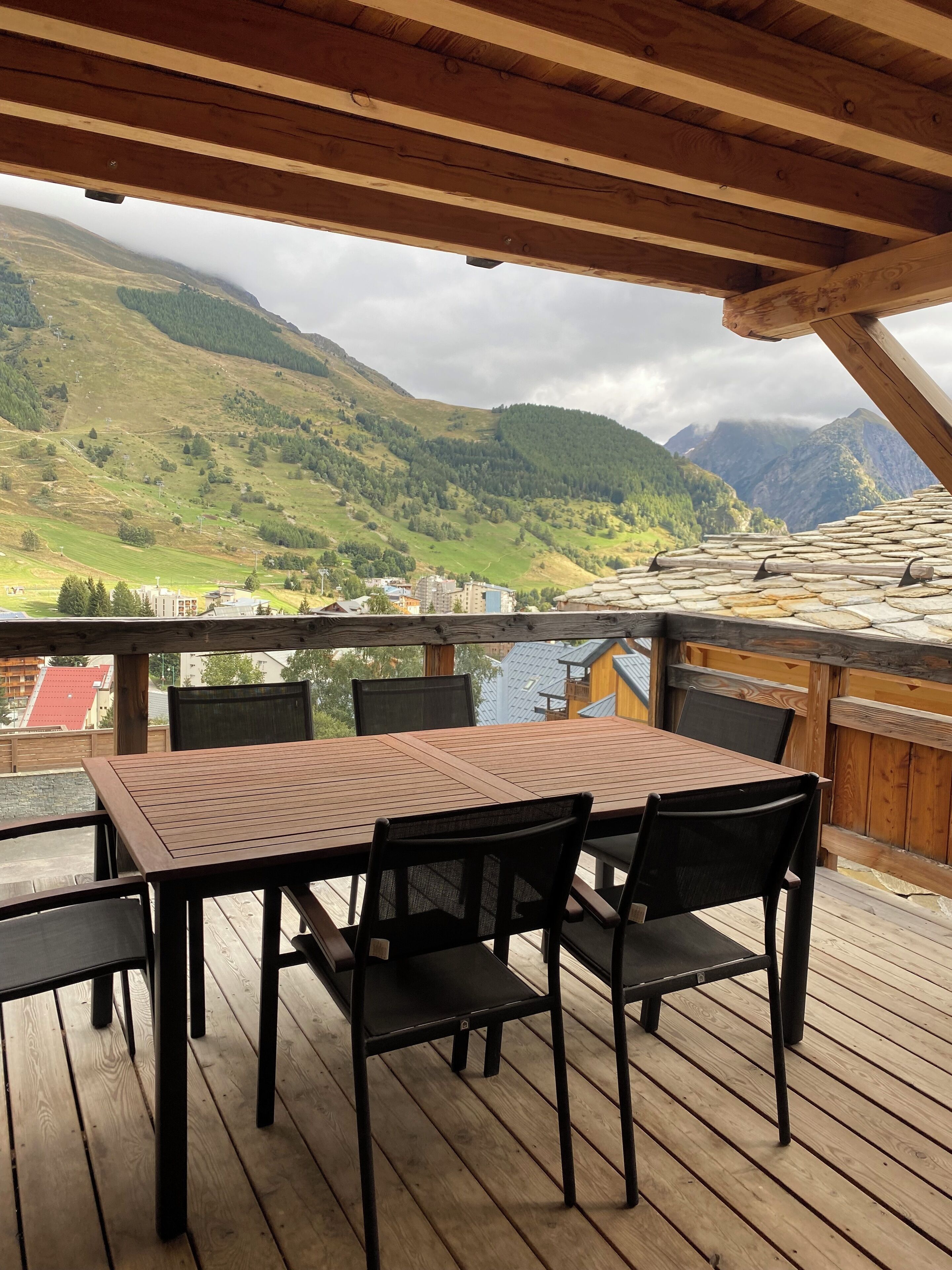 A wooden deck with a table and chairs, overlooking a mountainous landscape.