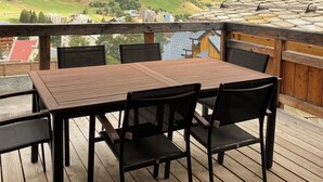 A wooden deck with a table and chairs, overlooking a mountainous landscape.