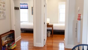 A hallway with two bedrooms, a bookshelf, and a small table with a lamp.