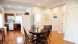 A spacious kitchen with wooden flooring, white cabinets, and a dining area with a round table and chairs.