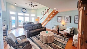 A spacious living room with a large sofa, a round coffee table, and a staircase leading to an upper level. - Ocean Breeze - 2nd Row, Best Sunrises, Surf Sounds (Freeport)