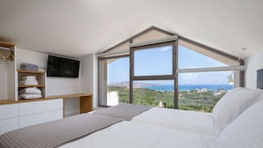 A bedroom with a large window, a bed, a TV, and a shelf with towels. - Kassiani Villa | Theo Luxury Villas With Sea View (Agia Marina)