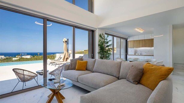 Un salon moderne doté d’une grande fenêtre, d’un canapé, d’une table basse en verre et offrant une vue sur la mer.