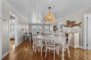 A dining area with a white table and chairs, a hanging light fixture, and a decorative fish wall art piece.