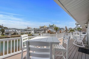 A wooden deck with white chairs and a table, overlooking a body of water and buildings.