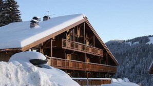 Una cabaña de madera con techo inclinado, varios balcones y un paisaje cubierto de nieve.