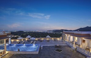 Ein Poolbereich auf dem Dach mit Liegestühlen und Sonnenschirmen mit Blick auf eine Stadtlandschaft in der Abenddämmerung.