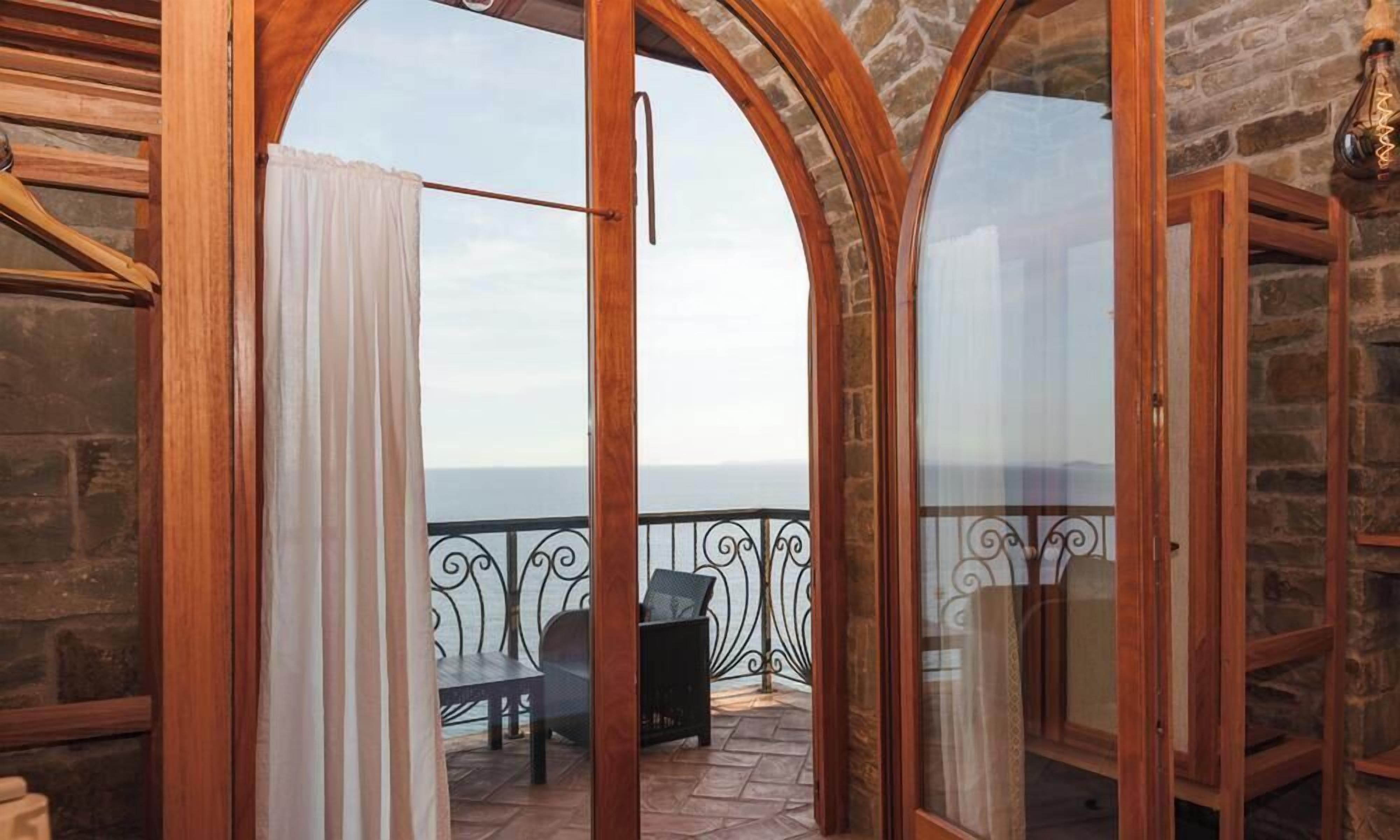 Une chambre avec vue sur la mer, un balcon avec une table et des chaises, et un mur en pierre.
