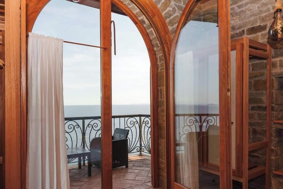 Una habitación con vistas al mar, un balcón con una mesa y sillas, y una pared de piedra.