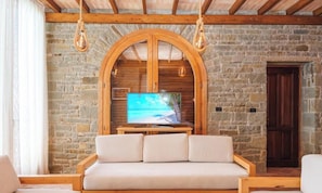 Une pièce aux murs de pierre, avec un meuble pour télévision en bois, un canapé et des luminaires suspendus.
