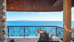 A covered outdoor area with a view of the sea, a black wrought iron railing, and a hammock. - Kshira Oasis Qeparo - Boutique Beachfront Suites & Restaurant (Himare)