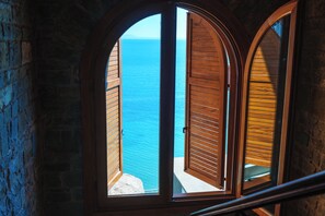 A view through an arched window with wooden shutters, overlooking a body of water. - Kshira Oasis Qeparo - Boutique Beachfront Suites & Restaurant (Himare)