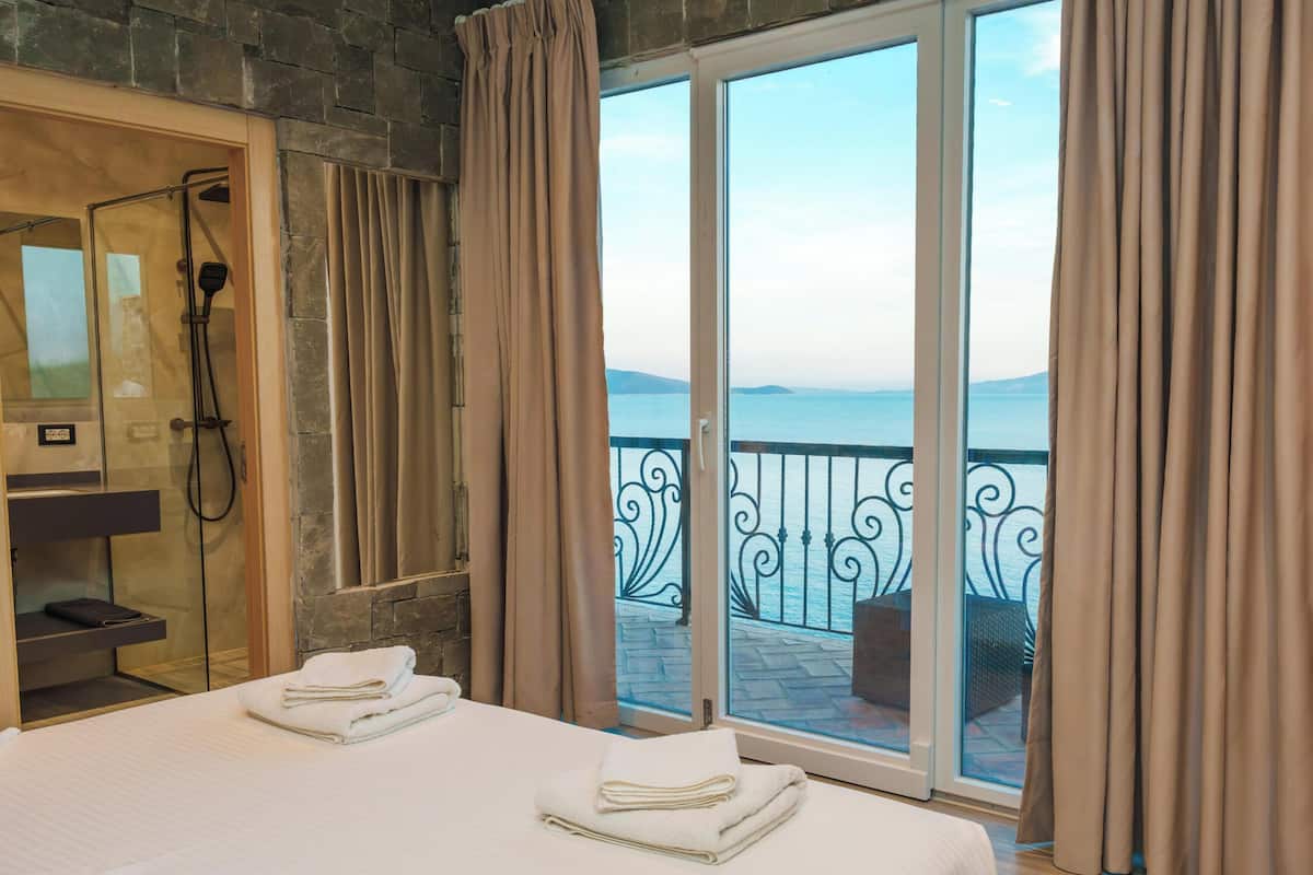 Habitación de hotel con cama, ducha y balcón con vista al mar.