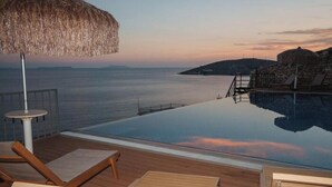 An infinity pool with a view of the sea, wooden deck, lounge chairs, and a thatched umbrella. - Kshira Oasis Qeparo - Boutique Beachfront Suites & Restaurant (Himare)