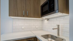 A modern kitchen with wooden cabinets, a stainless steel sink, and a microwave above the counter. - Mini Studio 2 by Grand Apartments (Sopot)