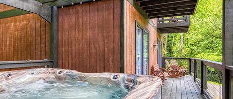 A hot tub on a wooden deck with a pergola overhead, surrounded by wooden walls and a view of greenery.